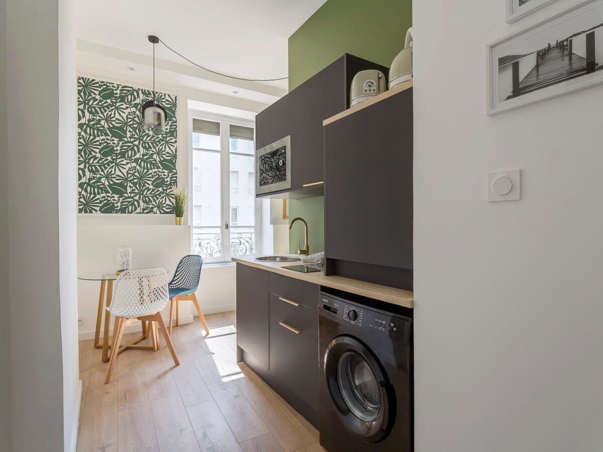 Cuisine linéaire anthracite à plan décor chêne, robinet laiton et lave-linge, ouverte sur un coin repas lumineux, Vaulx-en-Velin