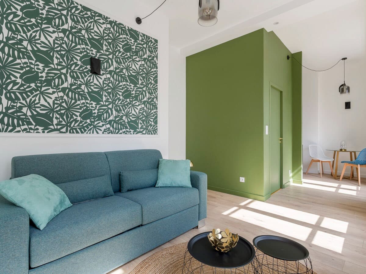 Séjour rénové à Vaulx-en-Velin : canapé bleu canard, panneau de papier peint tropical vert et volume cloisonné peint vert olive