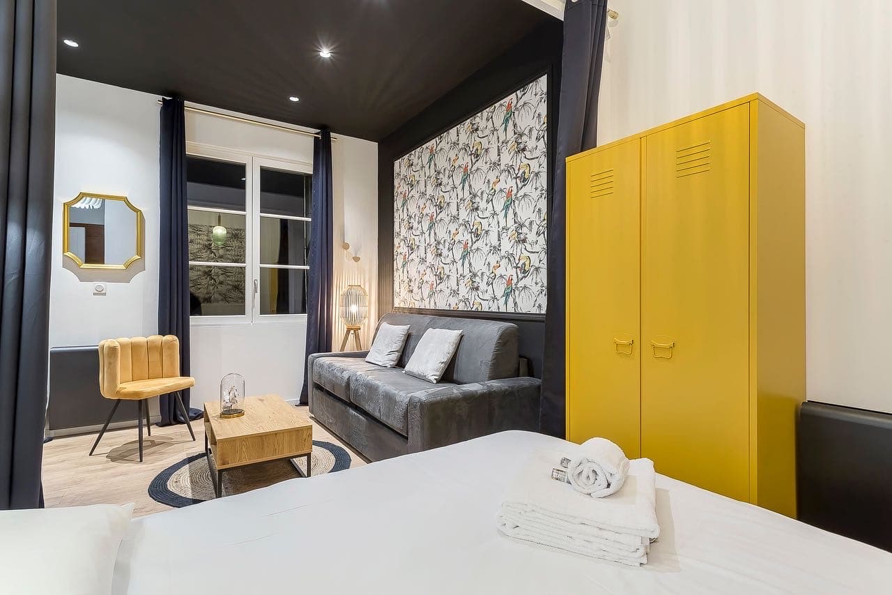 Studio rénové à Bourgoin-Jallieu : plafond noir à spots encastrés, papier peint perroquets derrière le canapé et armoire jaune